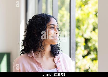 Smiling woman looking out window, enjoying peaceful moment at home Stock Photo