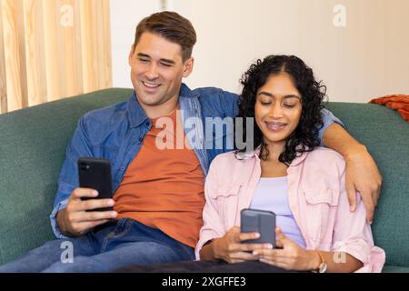 Young couple sitting on couch, using smartphones and smiling together Stock Photo