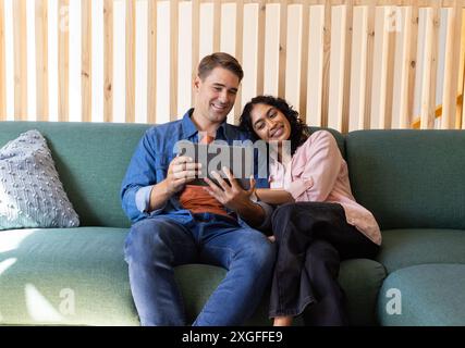 Young couple sitting on couch, smiling and using tablet together Stock Photo