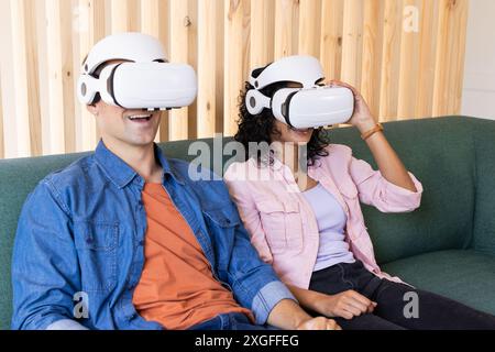 Using VR headsets, young couple sitting on couch and enjoying virtual reality Stock Photo