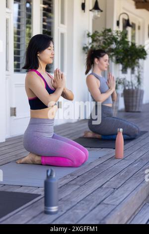Practicing yoga, two women friends meditating on yoga mats with water bottles nearby Stock Photo