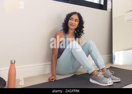 Sitting on yoga mat, woman in activewear resting after workout, smiling, copy space Stock Photo