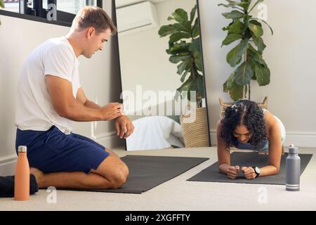 Man coaching woman doing plank exercise on yoga mat at home gym Stock Photo