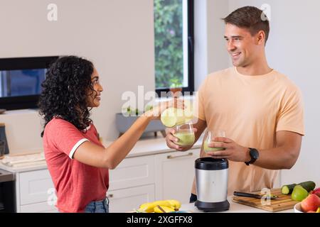 Making smoothies together, young couple pouring green juice in kitchen Stock Photo