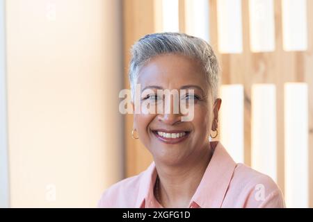 Smiling senior woman in casual shirt, looking at camera, indoors Stock Photo