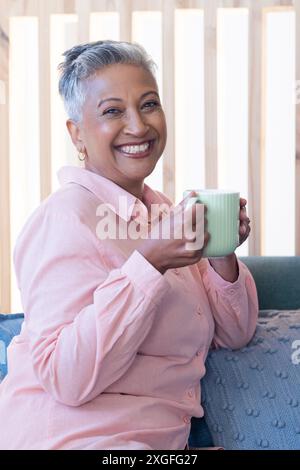 Smiling senior woman holding coffee mug, relaxing on couch at home Stock Photo