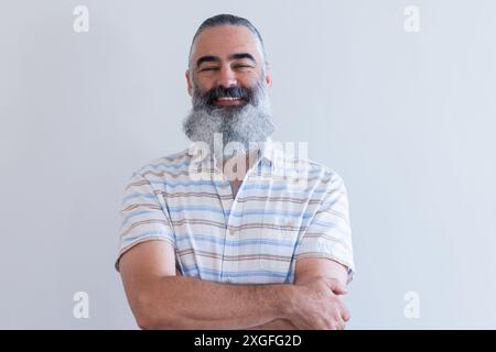 Smiling senior man with arms crossed, wearing striped shirt, looking confident Stock Photo