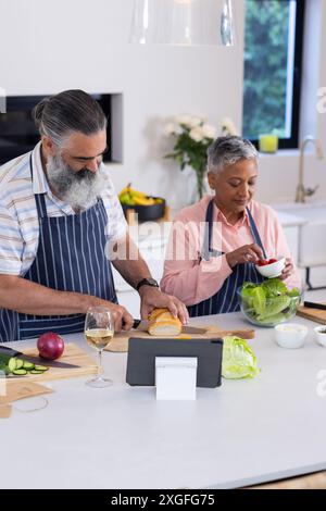 Preparing meal, senior couple chopping vegetables and using tablet in kitchen Stock Photo