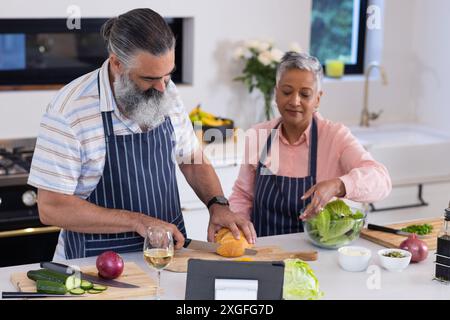 Chopping vegetables and using tablet, senior couple preparing meal together in kitchen Stock Photo