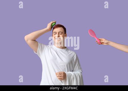 Young man with hair scalp massager and hand with brush on lilac background Stock Photo
