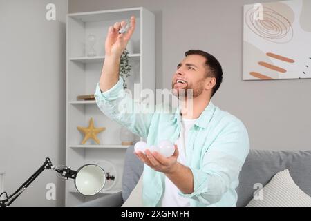 Young man choosing light bulbs for desk lamp at home Stock Photo
