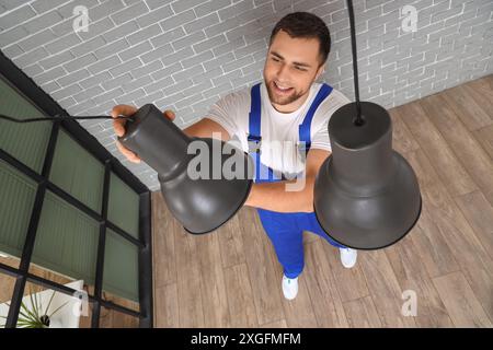 Male electrician changing light bulb in hanging lamp at home Stock Photo