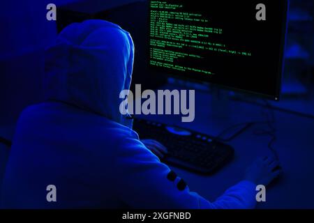 Hooded Figure Working on Computer in a Dark Room Stock Photo
