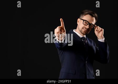 Young businessman in eyeglasses using virtual screen on black background Stock Photo
