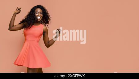 Happy Woman Wearing Pink Dress Dancing Against Peach Background Stock Photo