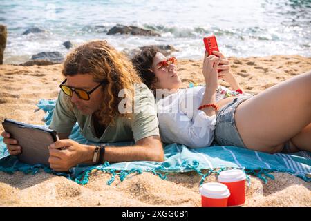 couple on the beach browsing smartphones,and tablet apps. Stock Photo