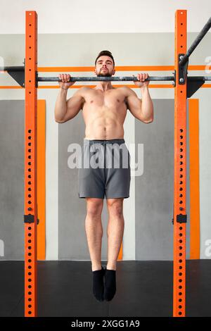 Muscular man hanging on bar and performing calisthenics pull up exercise in modern gym Stock Photo