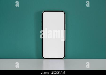 Smartphone with a blank screen standing on a white desk against a green wall is the perfect object for showcasing your mobile app or website design Stock Photo