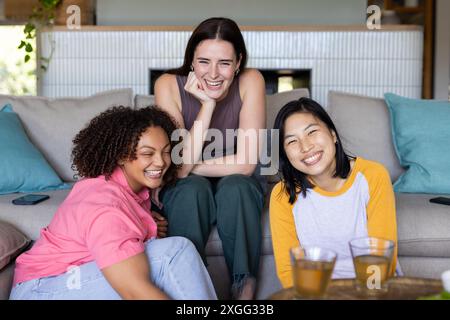 Smiling friends sitting on couch at home, enjoying drinks and spending time together Stock Photo