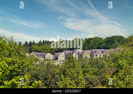 A scenic view of a new residential area (housing estate) surrounded by lush greenery and trees under a clear blue sky with houses with light-colored w Stock Photo