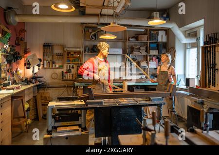 Cheerful married couple of carpenters fool around in creative workshop, having fun at workplace Stock Photo