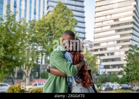 Joyful contented african american young man smiling hugging friend woman while nice meeting in city. Stock Photo