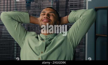 Relaxed satisfied businessman office manager employee resting dreaming at workplace taking break happy african american man holding hands behind head Stock Photo