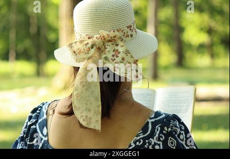 A woman with a hat is reading a book in the park Stock Photo