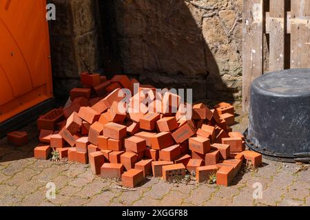 A pile of red bricks sits beside a building, resting on a patio made of pavers. Stock Photo