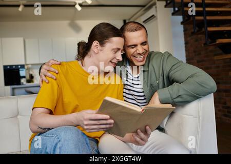 A young gay couple shares a laugh while reading a book together in a modern apartment. Stock Photo