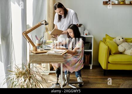 A mother helps her daughter with her schoolwork while she sits at a desk. The daughter is wearing a prosthetic leg. Stock Photo