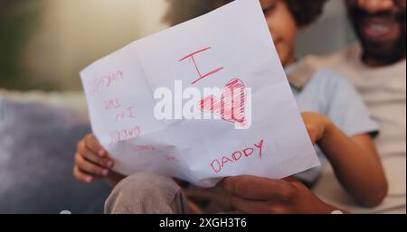 Dad, letter and relax with son for love, heart or present on sofa for fathers day surprise at home. Papa, child or little boy reading note of Stock Photo