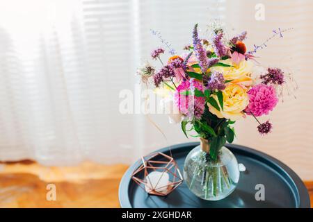Top view of fresh summer bouquet put in transparent vase on table. Pink, yellow, purple blooms. Floral arrangement at home made of dahlias, roses, ver Stock Photo