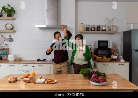 Lively middle-aged family couple dancing to disco music in the kitchen.Happy old man and woman having fun, entertaining together in the house, partici Stock Photo
