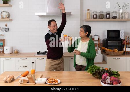 Beautiful playful senior couple in aprons dancing and smiling while preparing healthy dinner at home. A beautiful senior couple is dancing and smiling Stock Photo