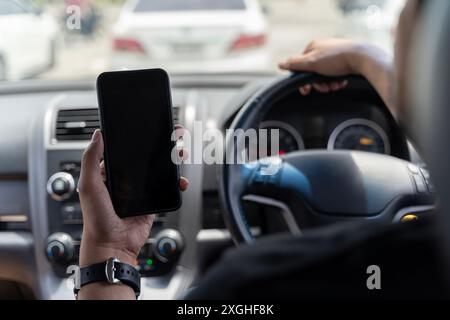 Mock up of man using mobile smart phone inside a car. Driver hand holding blank black screen smartphone, searching address and pin location via map na Stock Photo