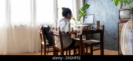 Professional businesswoman working at her home on laptop, young female manager using mobile computer device while sitting at dining table, work proces Stock Photo