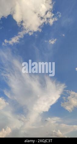 White fluffy clouds moving across a clear blue sky. Vertical mobile photo. sstkvertical Stock Photo