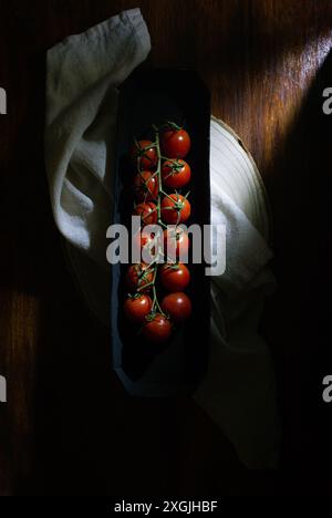 Low key still life. A closeup of a tray of tomatoes. The tray is on a wooden table and the tomatoes are arranged in a row. The image has a warm Stock Photo