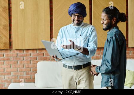 Two Indian colleagues standing in office waiting zone while one of them showing presentation, thrilled and full of enthusiasm Stock Photo