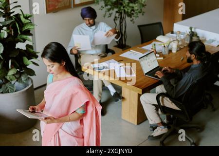 High angle shot of small group of IT specialist working with diagrams and database using different digital devices and sources of information Stock Photo