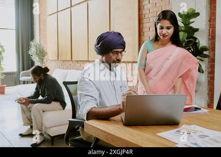 Indian colleagues discussing last financial statistics while one of them chilling on sofa in blurred background Stock Photo