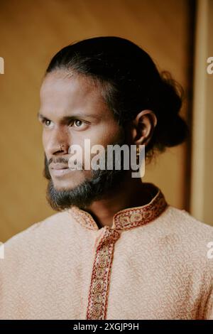 Medium close up of young brutal Indian man with golden nose ring and earring looking away Stock Photo