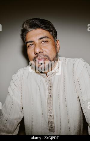 Medium close up of middle aged Indian man dressed in flax robe with red patterns looking directly with squint Stock Photo