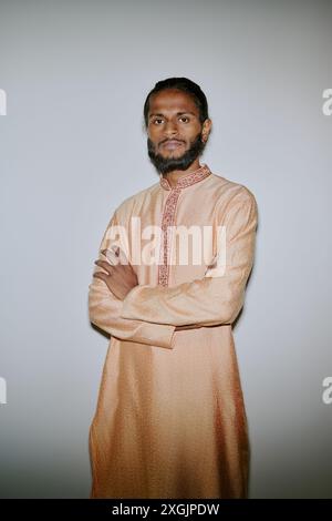 Portrait of young confident Indian businessman dressed in patterned pastel peach colored robe crossing arms while looking directly at camera Stock Photo