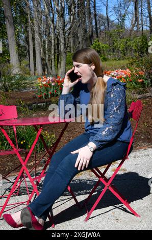 Young woman sits in a garden in Memphis, Tennessee.  She is talking on her phone and seems to be having an argument.  She has on a blue shirt and jean Stock Photo