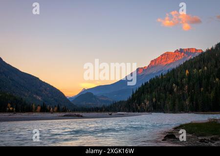 Majestic mountain range is glowing in the warm light of the setting sun, while a serene river flows through a valley Stock Photo
