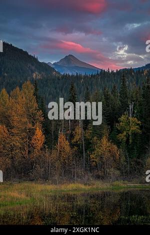 Mountain lake and pine forest are illuminated by the setting sun reflecting off dramatic pink and purple clouds Stock Photo