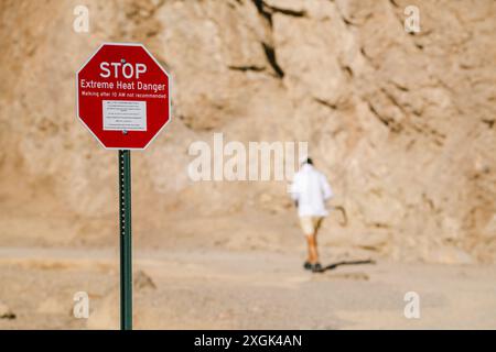 A man is walking in a desert with a stop sign in front of him. The sign warns of extreme heat danger Stock Photo