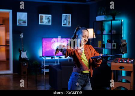 Youngster joins viral dance craze inspired by beloved celebrities, recording family friendly video with smartphone on selfie stick. Cheerful child does latest internet dancing challenge Stock Photo